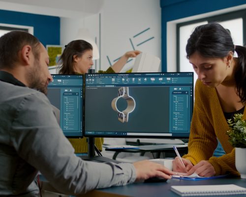 Team discussing about industrial project using dual monitors setup to desing 3D gears and metalic clamp in CAD software. Industrial engineer and african project manager working together in creative office